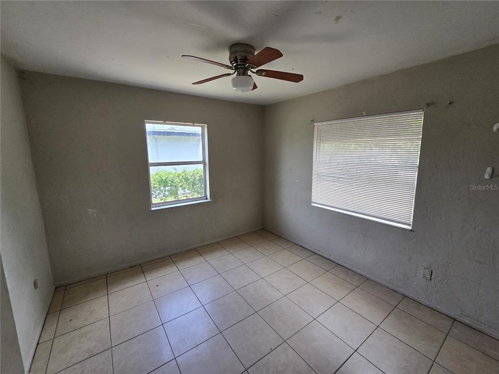 An empty bedroom features beige tile flooring, light-colored walls, a ceiling fan, and two windows — 1511 27TH STREET S, ST PETERSBURG, FL