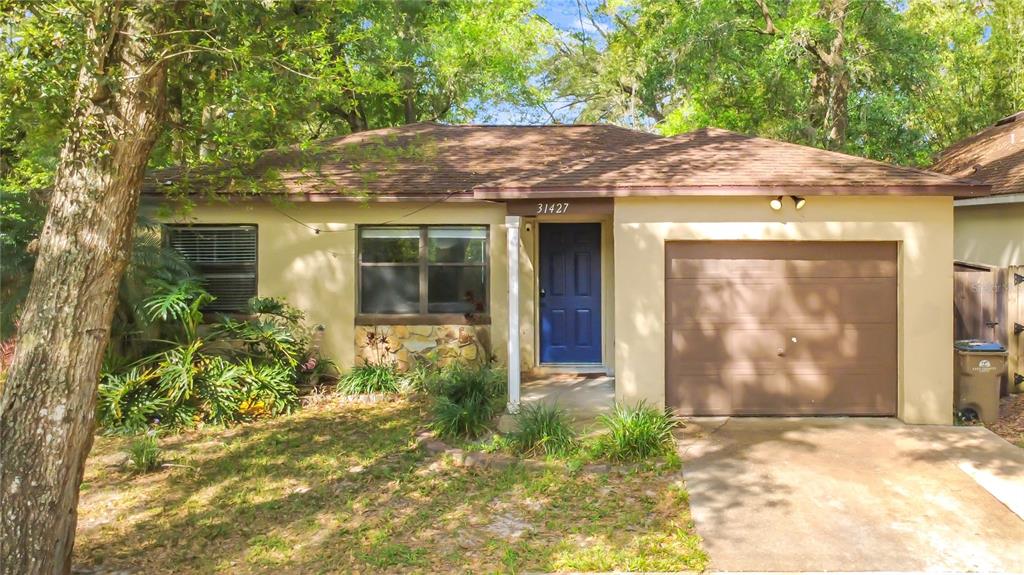 A single-story house with a brown roof, tan stucco exterior, blue door, and attached garage — 31427 GHENT AVENUE, MOUNT PLYMOUTH, FL