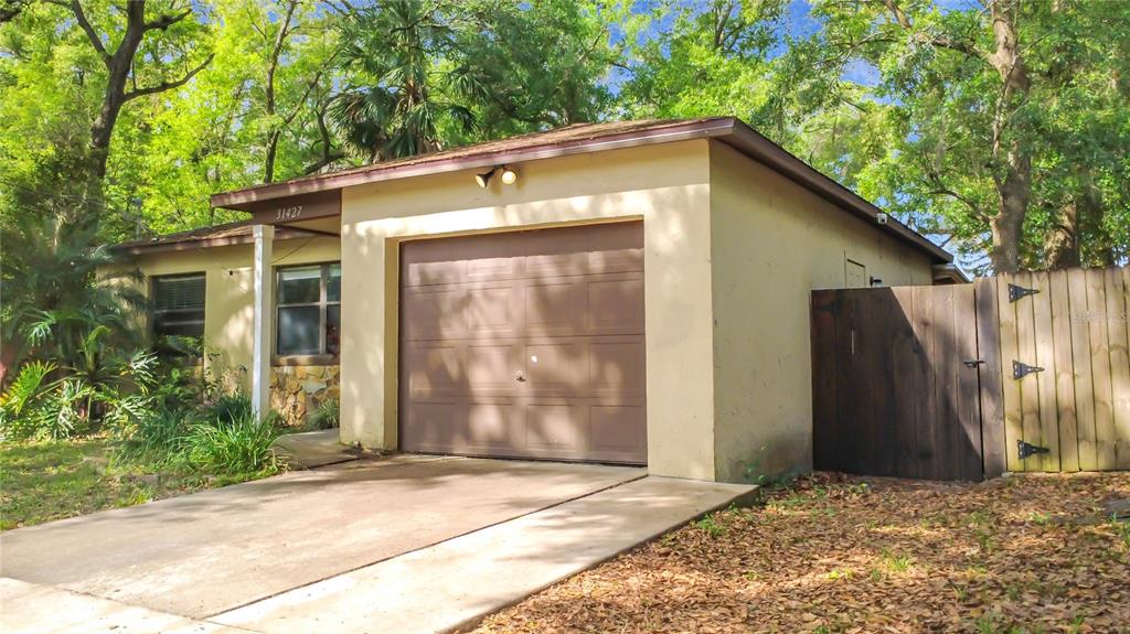 A single-story house exterior features a beige stucco facade, a garage, and a wooden fence — 31427 GHENT AVENUE, MOUNT PLYMOUTH, FL