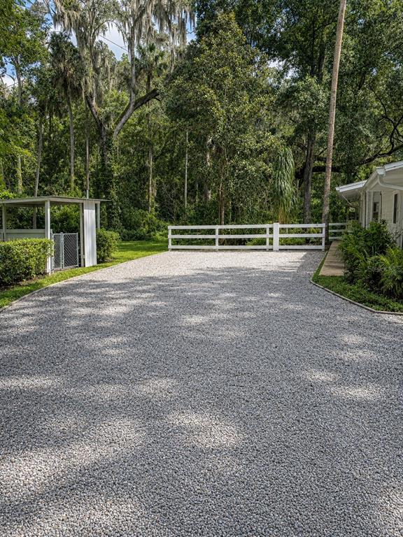 A gravel driveway leads toward a white fence and a small covered structure near trees — 1735 TIMOCUAN WAY UNIT A, LONGWOOD, FL