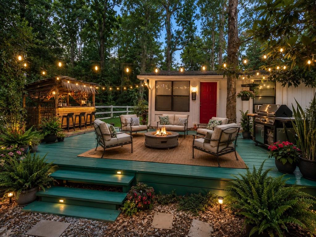 A teal wooden deck features a fire pit, outdoor seating, a tiki bar, and string lights — 1735 TIMOCUAN WAY UNIT A, LONGWOOD, FL