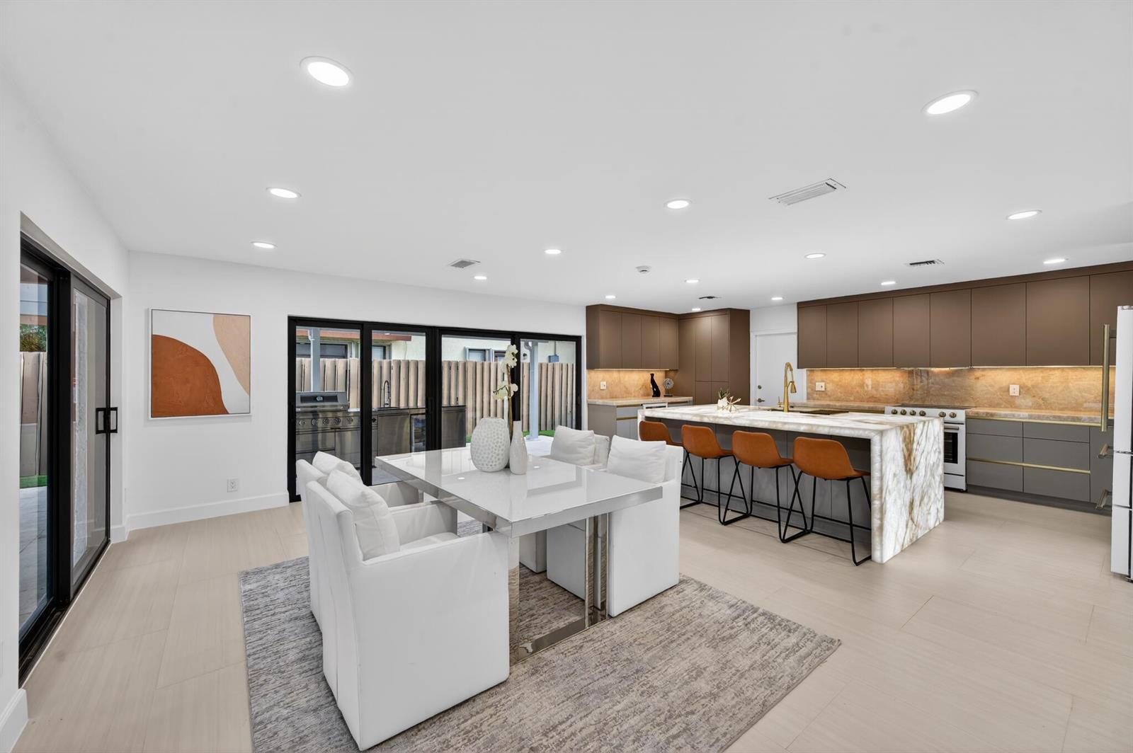 A modern kitchen and dining area with a marble island, brown cabinetry, and sliding doors — 3088 NW 26th Avenue, Boca Raton FL 33434, BOCA RATON, FL