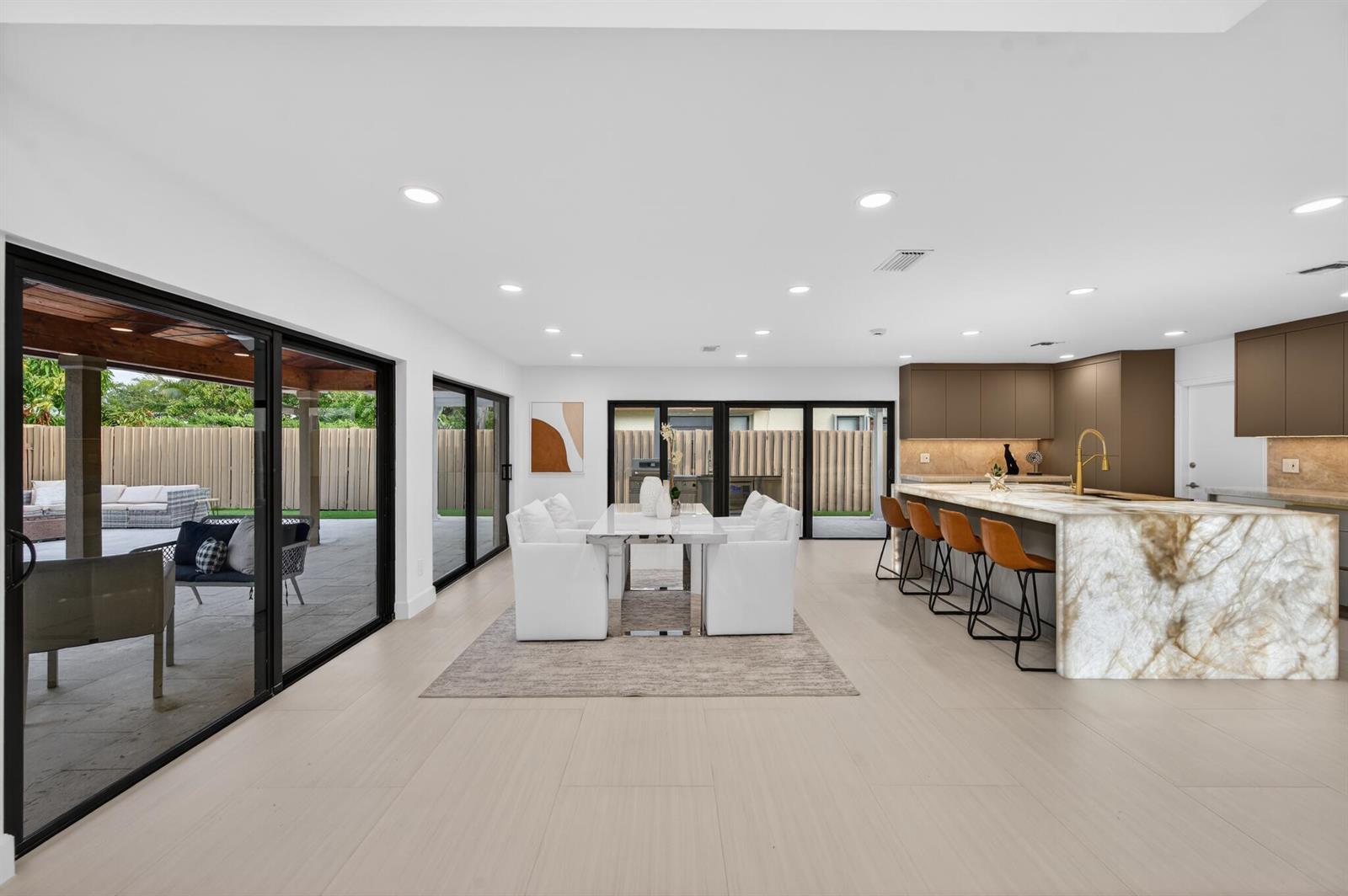 A modern open-concept kitchen and dining area features a large marble island and sliding glass doors — 3088 NW 26th Avenue, Boca Raton FL 33434, BOCA RATON, FL