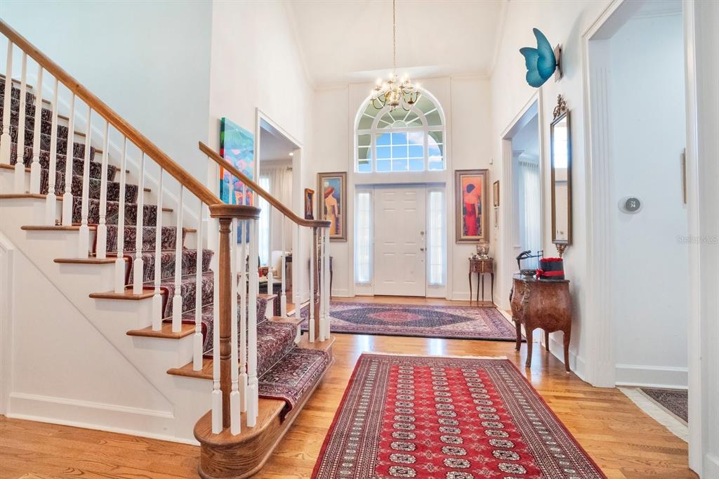 A grand foyer features a staircase with a patterned runner, hardwood floors, and area rugs — 1451 HOLLINGSWORTH OAKS DRIVE, LAKELAND, FL
