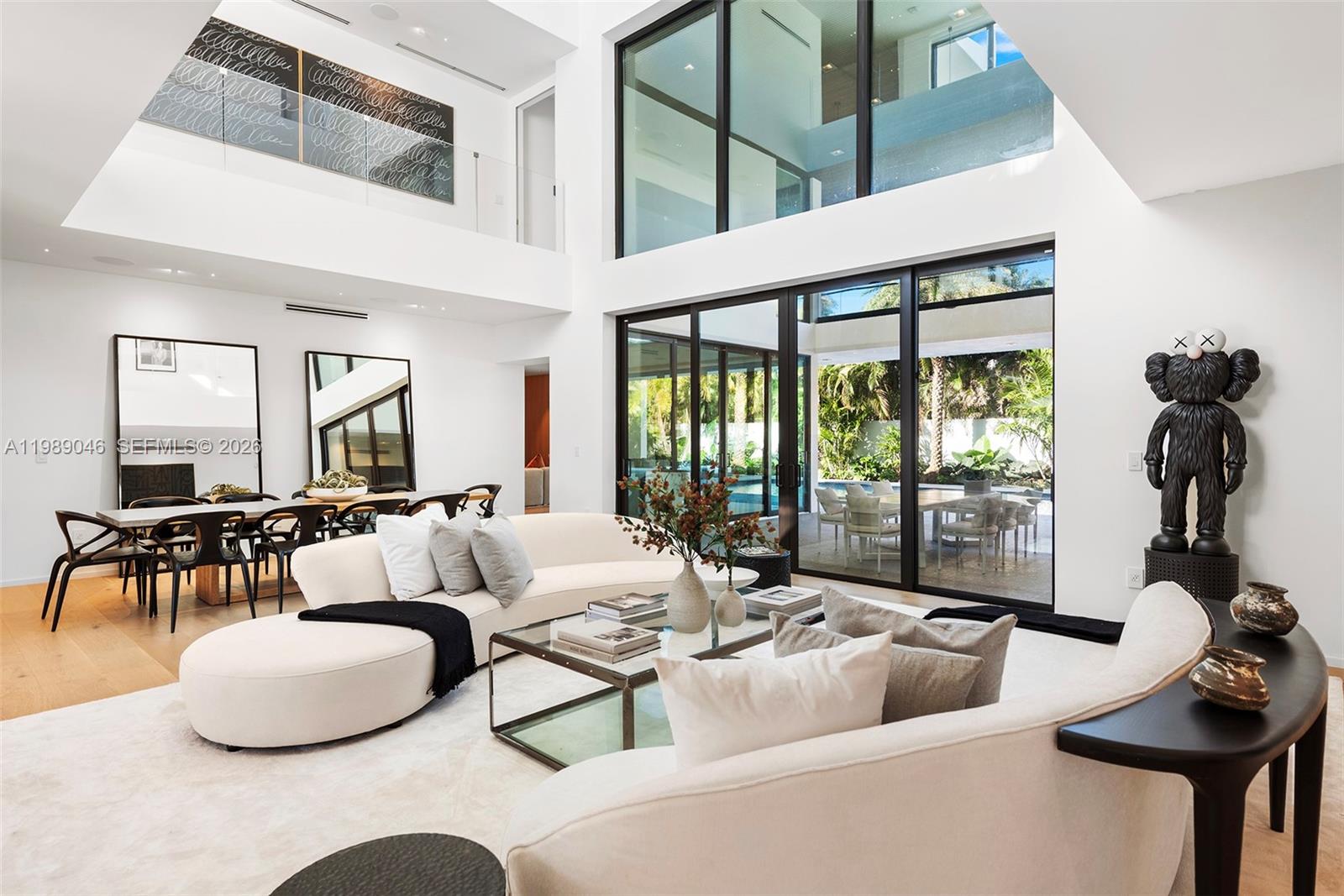 A modern living room features high ceilings, floor-to-ceiling windows, and a curved white sofa — 128 Ocean Blvd, Golden Beach FL 33160, GOLDEN BEACH, FL