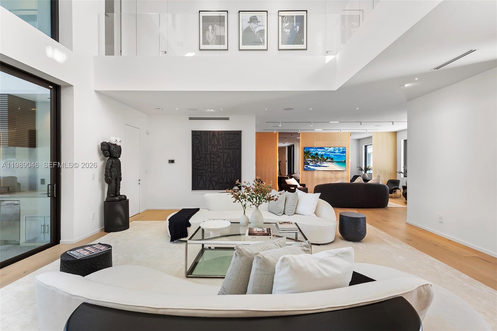 A modern, high-ceilinged living room features white sofas, a glass coffee table, and black artwork — 128 Ocean Blvd, Golden Beach FL 33160, GOLDEN BEACH, FL
