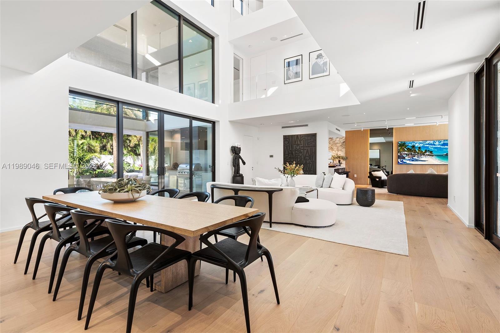 A modern, open-concept living and dining area features high ceilings, light wood floors, and floor-to-ceiling windows — 128 Ocean Blvd, Golden Beach FL 33160, GOLDEN BEACH, FL
