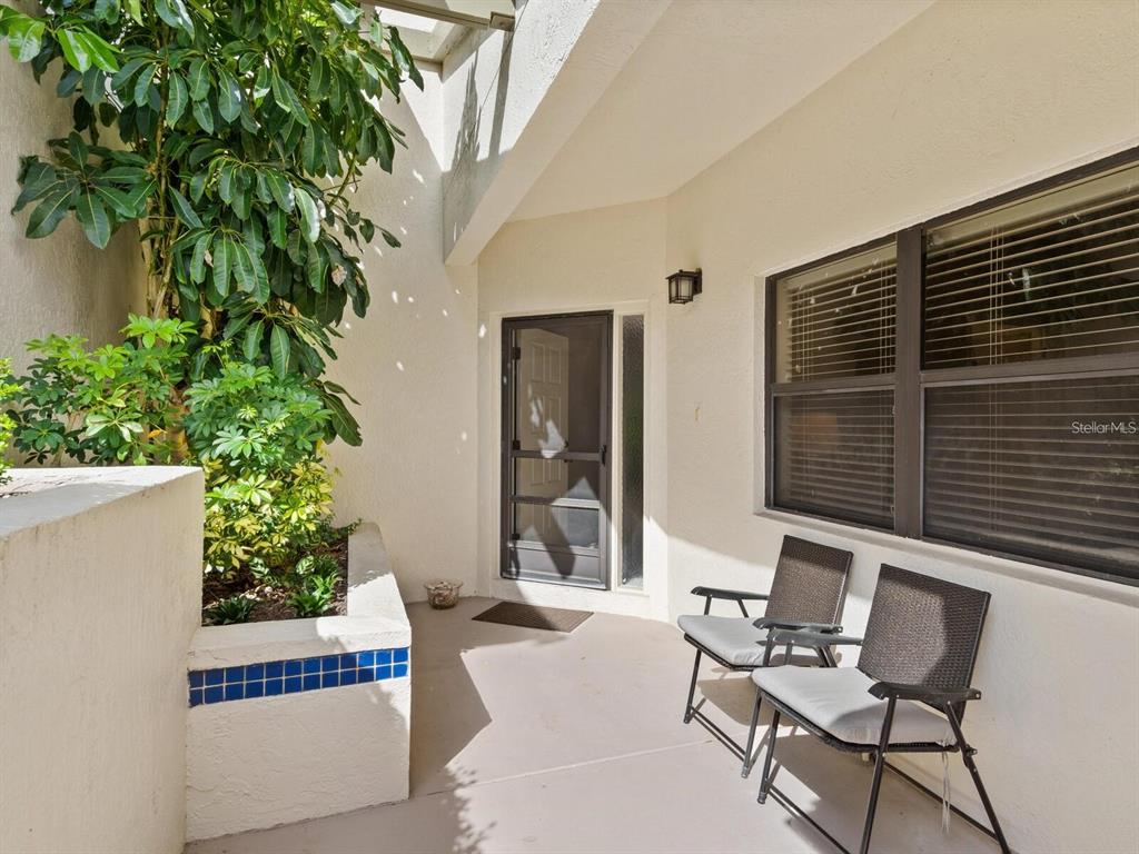 A patio features a small planter, two chairs, and a screen door entrance — 1678 STARLING DRIVE UNIT 102, SARASOTA, FL