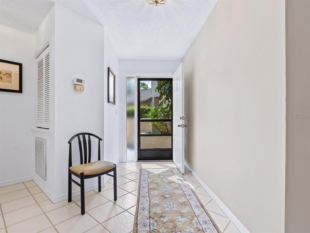 An entryway features a tiled floor, a runner rug, a chair, and an open door — 1678 STARLING DRIVE UNIT 102, SARASOTA, FL