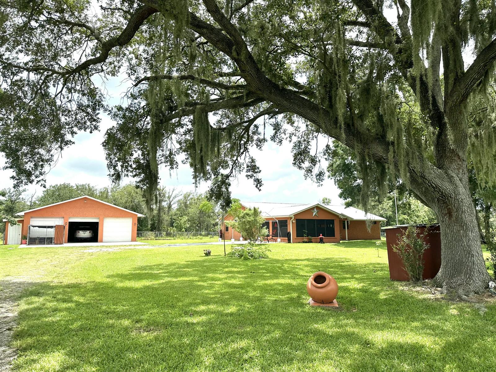A large orange house and detached garage sit on a grassy lawn under oak trees — 840 NW 141st Street, Okeechobee FL 34972, OKEECHOBEE, FL