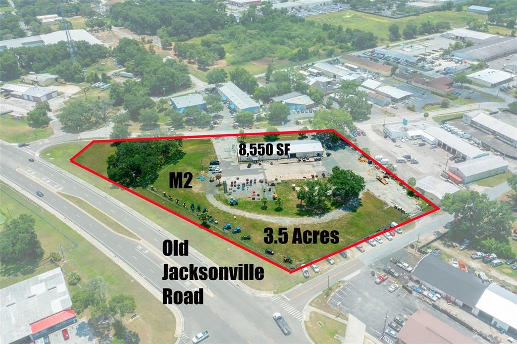 An aerial view shows a fenced commercial lot with a building and trees on 3.5 acres — 1904 NE JACKSONVILLE ROAD, OCALA, FL