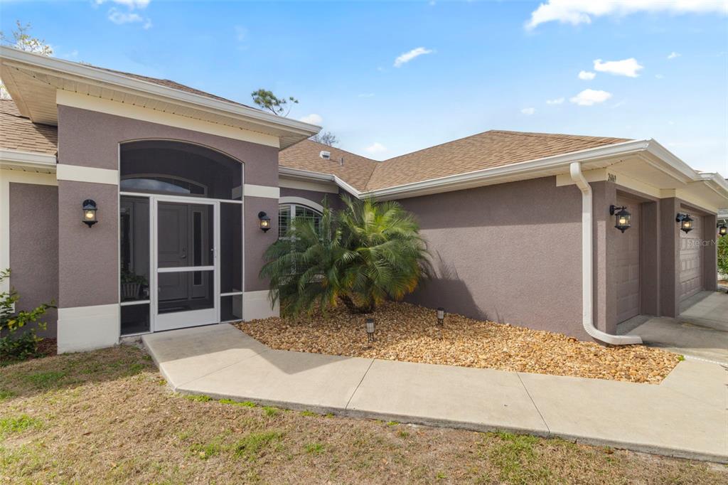 A single-story house exterior features a covered entryway, a palm tree, and a garage — 26069 PARANA DRIVE, PUNTA GORDA, FL