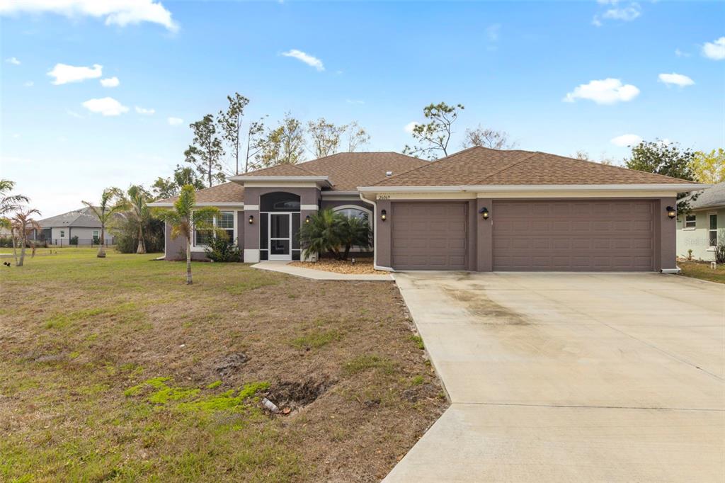 A single-story house with a brown exterior, a three-car garage, and a concrete driveway — 26069 PARANA DRIVE, PUNTA GORDA, FL