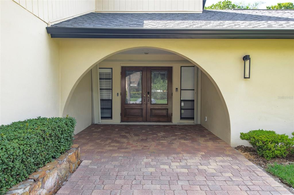 A brick-paved entryway features a large arched alcove leading to double wooden front doors — 3119 HYDE PARK DRIVE, CLEARWATER, FL