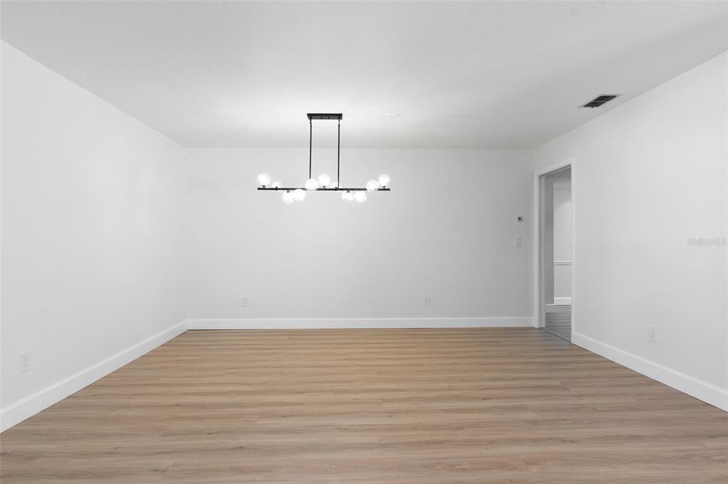 An empty room with light wood-look flooring, white walls, and a modern globe chandelier — 3119 HYDE PARK DRIVE, CLEARWATER, FL