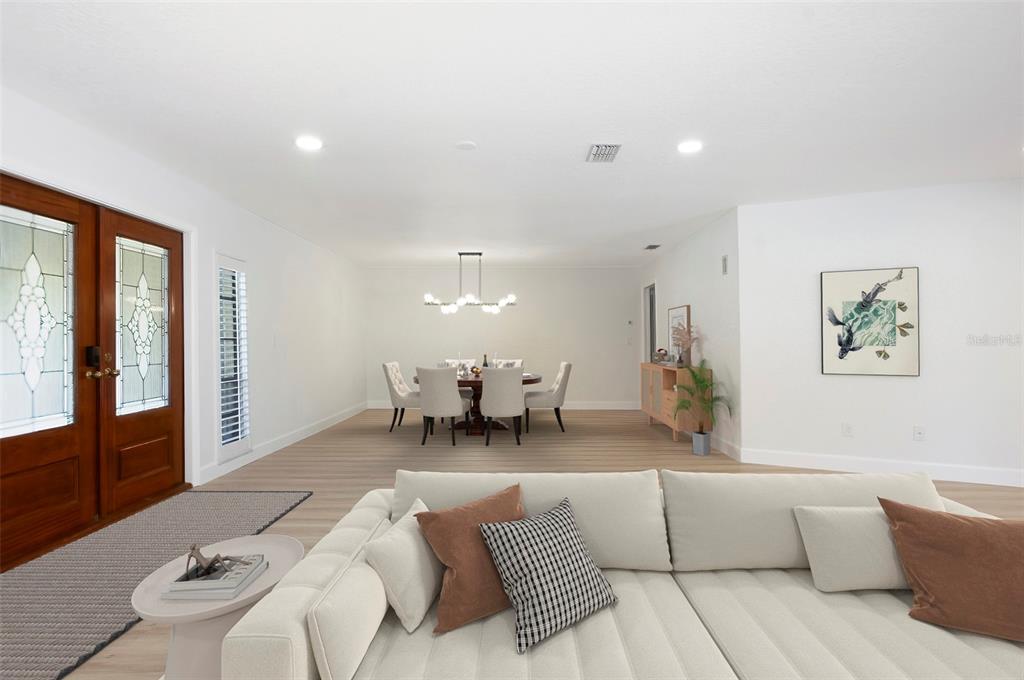 A bright living room with a white sectional sofa faces a dining area with light flooring — 3119 HYDE PARK DRIVE, CLEARWATER, FL