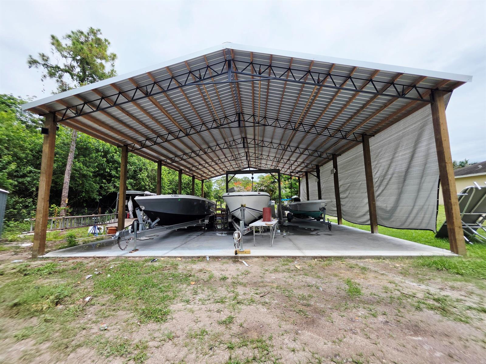 A large metal-roofed carport shelters three boats parked on a concrete slab — 17331 38th Road N, FL 33470, FL