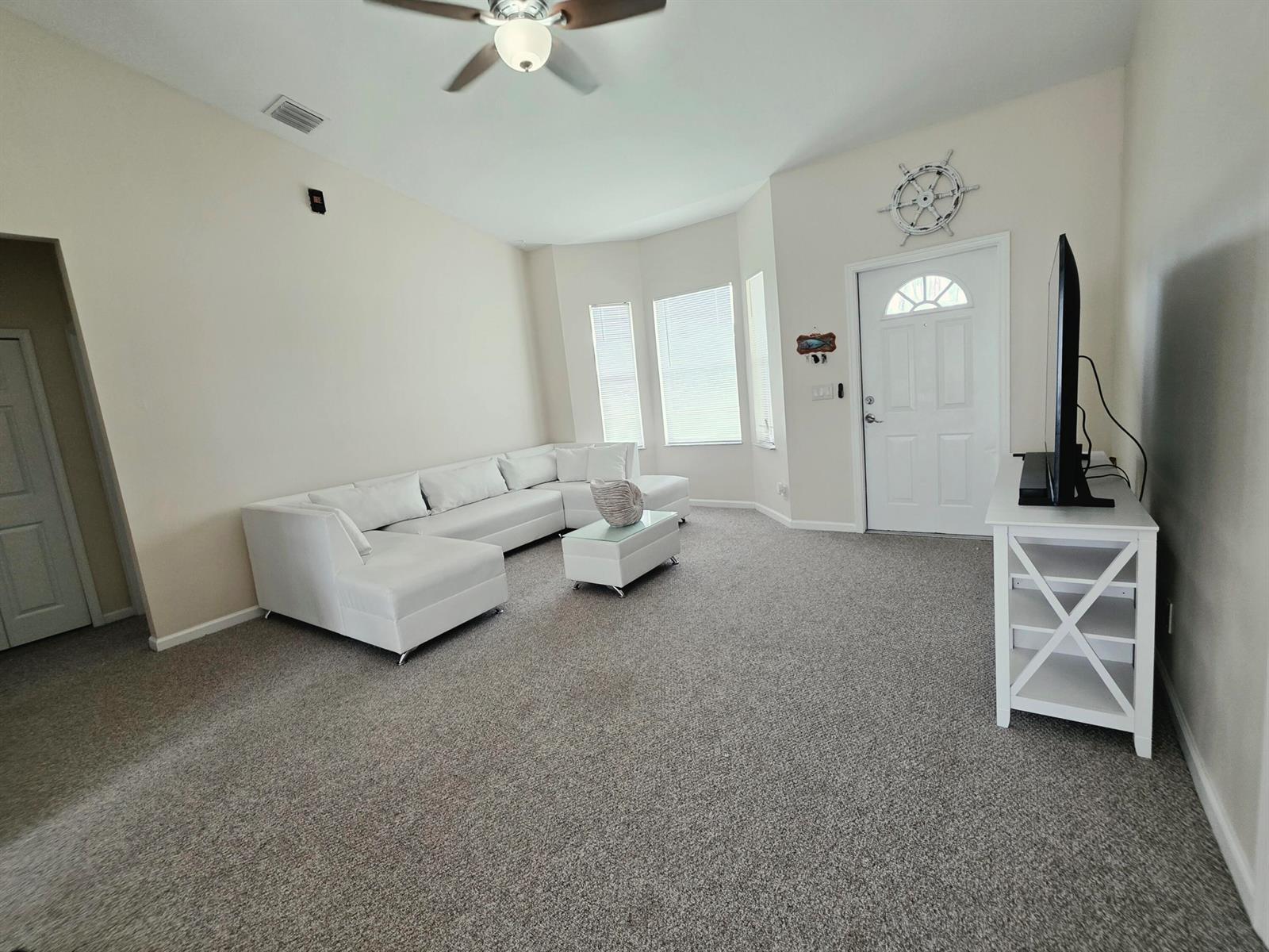 A living room features a white sectional sofa, a matching coffee table, and gray carpeting — 17331 38th Road N, FL 33470, FL