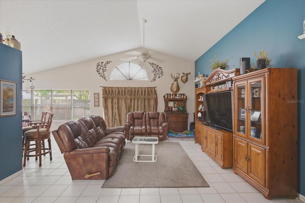 A living room with tile floors, vaulted ceilings, brown leather furniture, and a large entertainment center — 108 N BRISTOL CIRCLE, SANFORD, FL