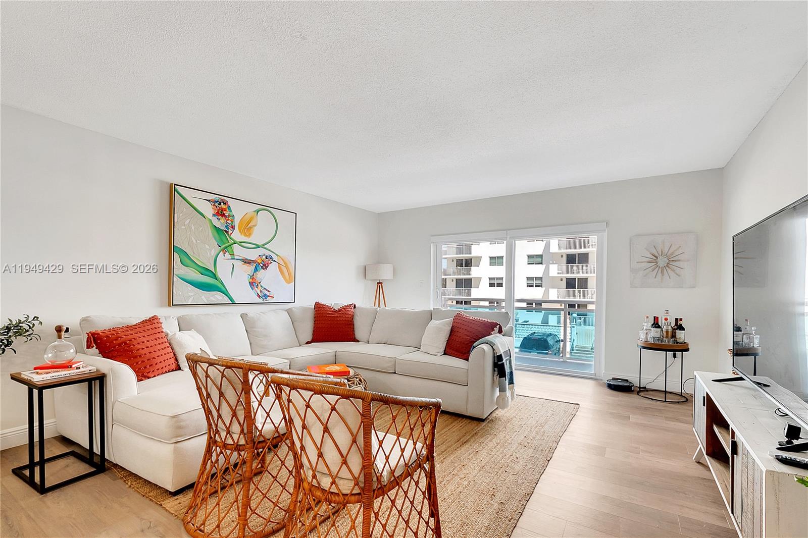 A living room features a white sectional sofa, two wicker chairs, and a large television — 1701 S Ocean Dr # 202, Hollywood FL 33019, HOLLYWOOD, FL