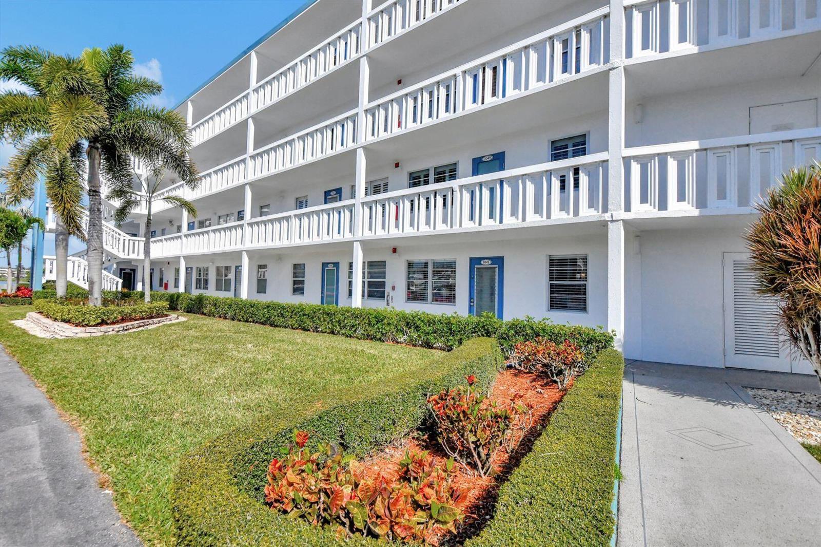 A multi-story white apartment building features exterior walkways, blue doors, and landscaped front lawns — 1047 Exeter C, Boca Raton FL 33434, BOCA RATON, FL