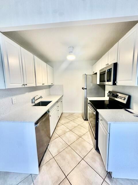 A galley kitchen features white cabinets, stainless steel appliances, and light-colored tile flooring — 1047 Exeter C, Boca Raton FL 33434, BOCA RATON, FL