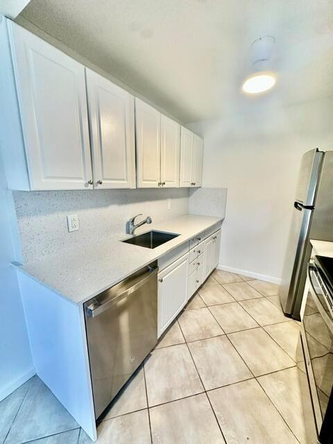 A kitchen features white cabinets, stainless steel appliances, and light-colored countertops with tile flooring — 1047 Exeter C, Boca Raton FL 33434, BOCA RATON, FL