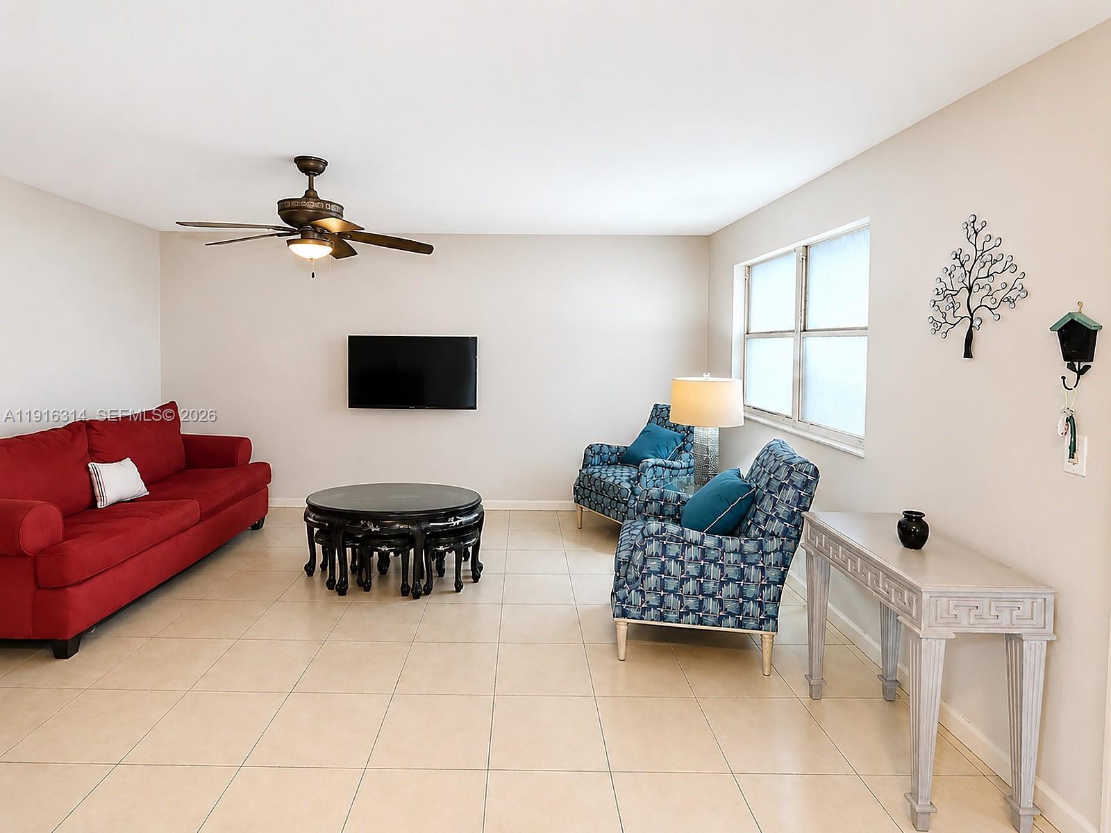 A living room features a red sofa, two blue patterned armchairs, and a round table — 116 Tuscany B # 116, Delray Beach FL 33446, DELRAY BEACH, FL