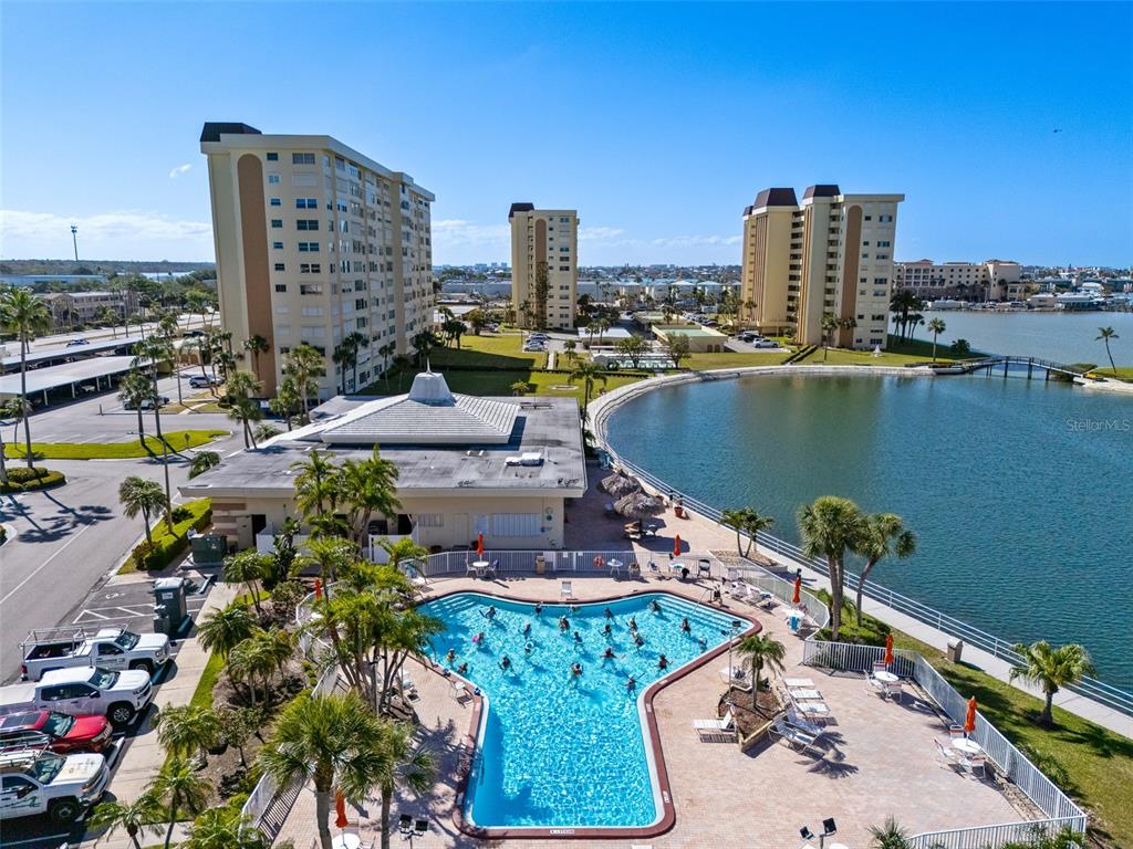An aerial view shows a swimming pool, a clubhouse, and tall residential buildings near water — 4775 COVE CIRCLE UNIT 103, ST PETERSBURG, FL