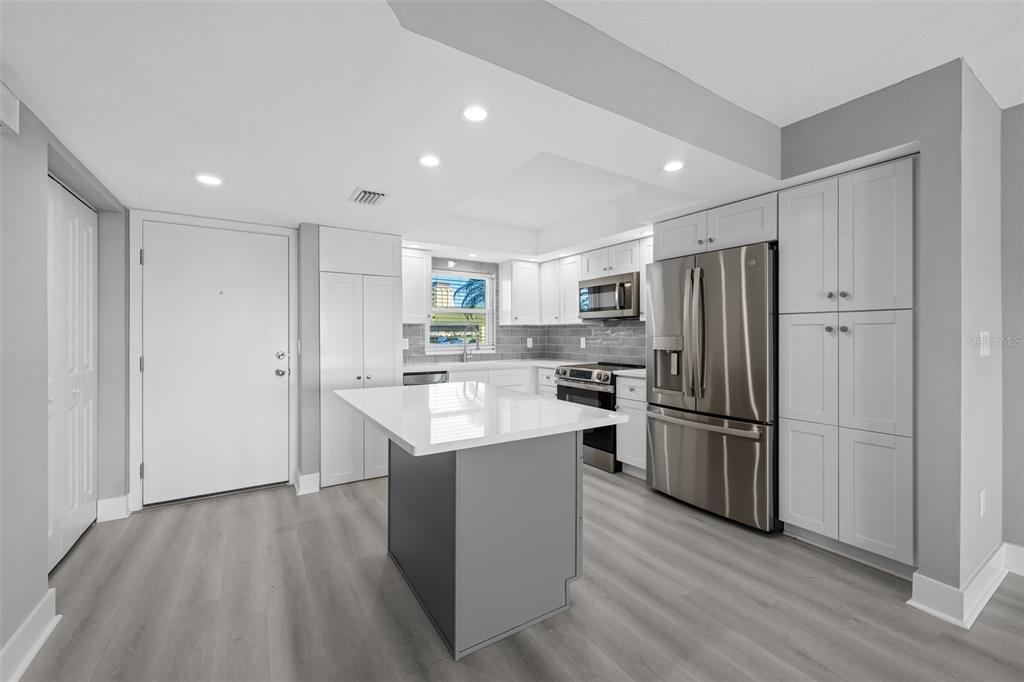 A modern kitchen features white cabinets, a gray island, stainless steel appliances, and wood-look flooring — 4775 COVE CIRCLE UNIT 103, ST PETERSBURG, FL