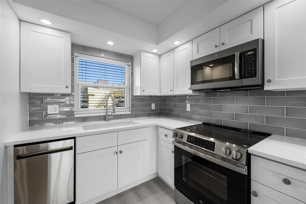 A modern kitchen features white cabinets, stainless steel appliances, and a gray subway tile backsplash — 4775 COVE CIRCLE UNIT 103, ST PETERSBURG, FL