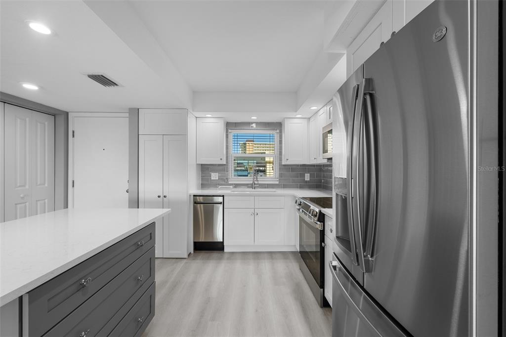 A modern kitchen features white cabinetry, stainless steel appliances, a gray island, and subway tile — 4775 COVE CIRCLE UNIT 103, ST PETERSBURG, FL