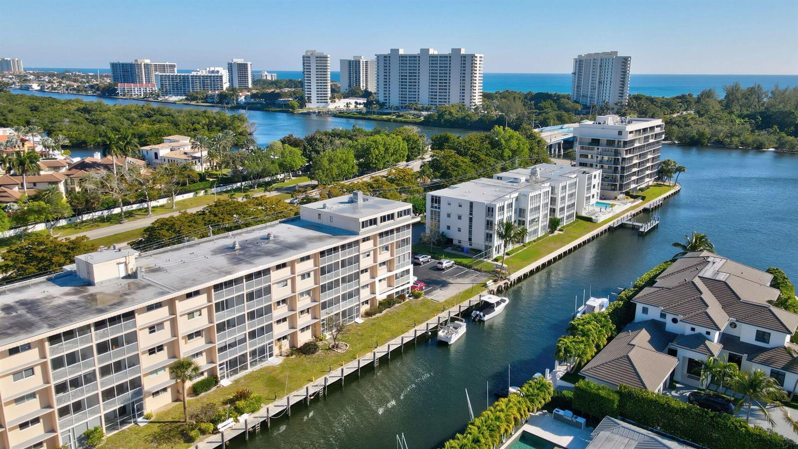 An aerial view shows multi-story apartment buildings situated along a canal near the ocean — 750 NE Spanish River Boulevard # 201, Boca Raton FL 33431, BOCA RATON, FL