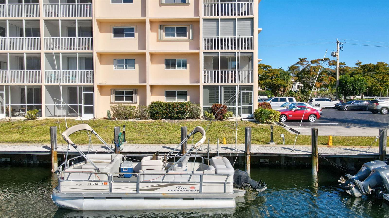 A pontoon boat is docked in front of a multi-story apartment building with a parking lot — 750 NE Spanish River Boulevard # 201, Boca Raton FL 33431, BOCA RATON, FL