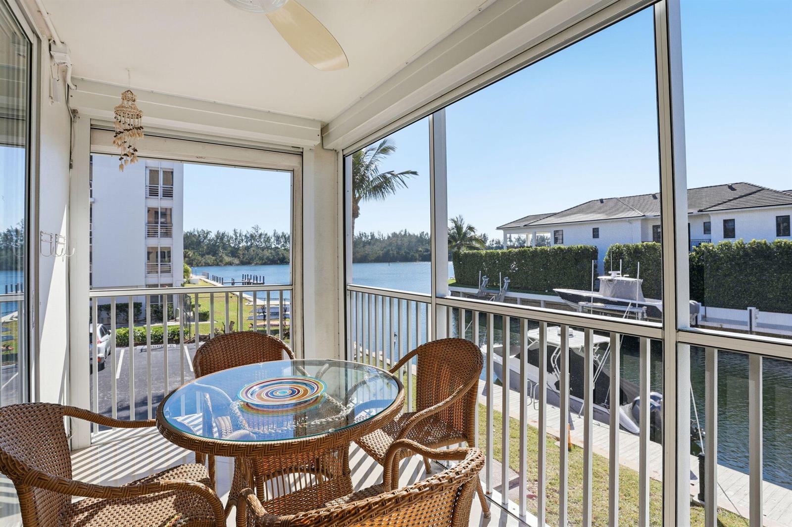 A screened-in balcony features wicker furniture and a glass table overlooking a canal with boats — 750 NE Spanish River Boulevard # 201, Boca Raton FL 33431, BOCA RATON, FL