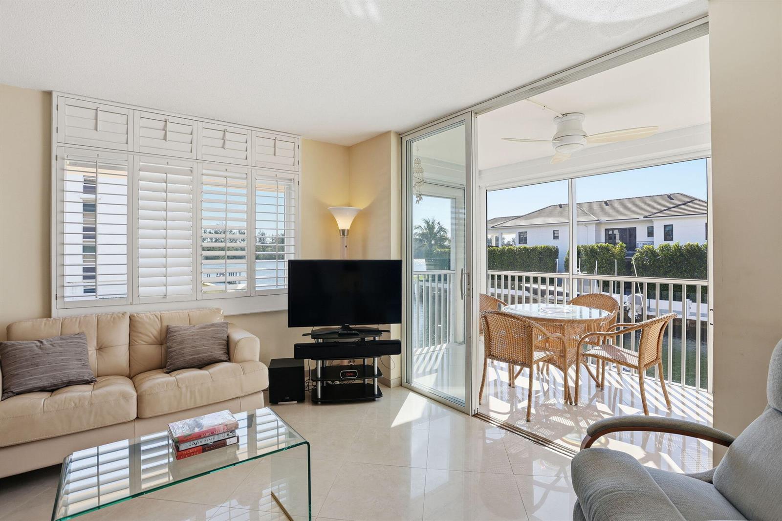 A living room with a beige sofa, glass coffee table, and sliding doors to a balcony — 750 NE Spanish River Boulevard # 201, Boca Raton FL 33431, BOCA RATON, FL