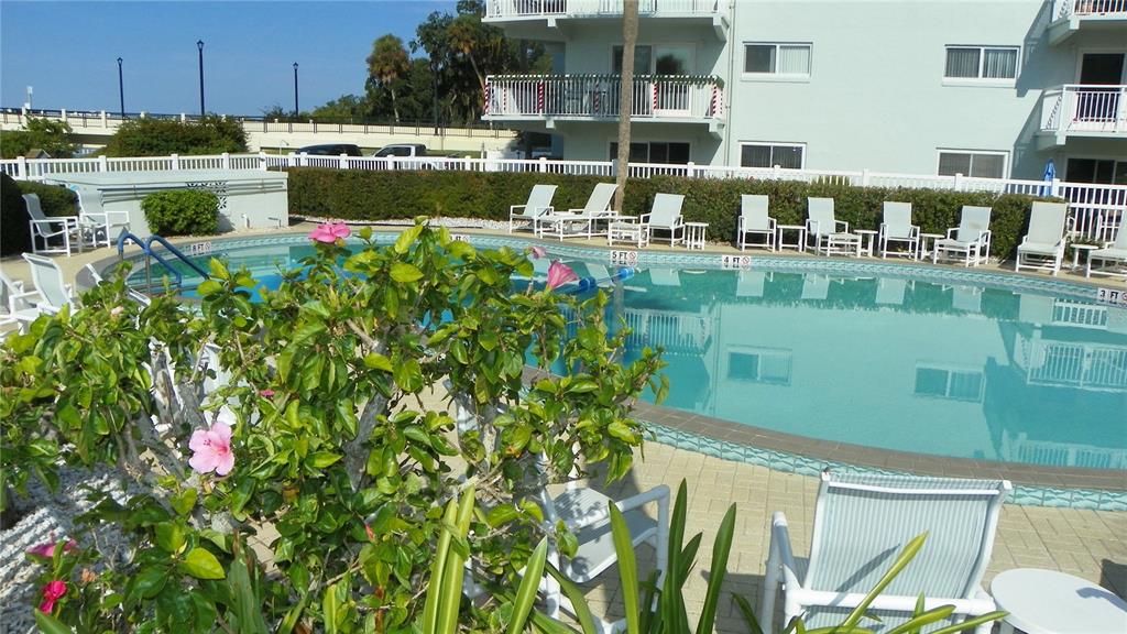 A swimming pool with lounge chairs sits in front of a multi-story apartment building — 100 SILVER BEACH AVENUE UNIT 214, DAYTONA BEACH, FL