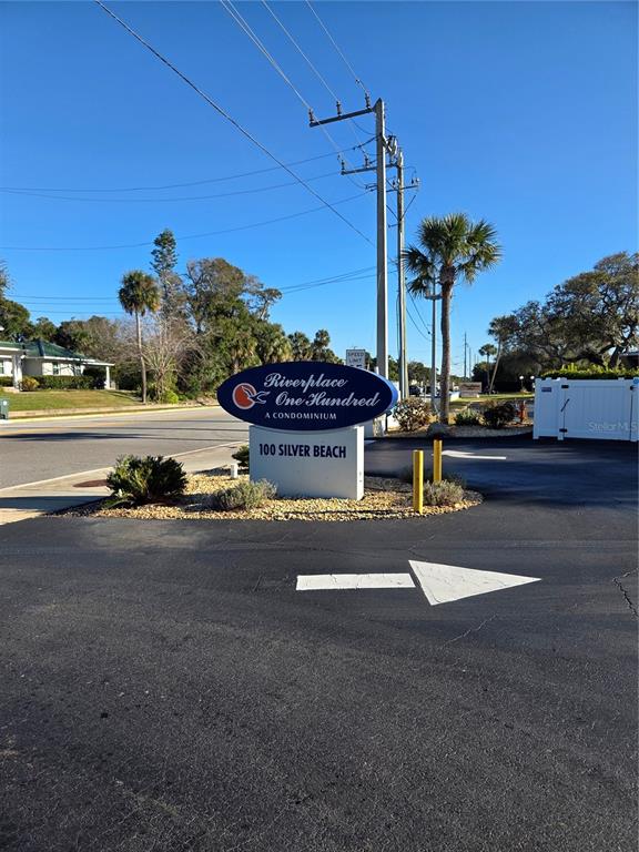 A blue sign for Riverplace One Hundred stands at the entrance of a paved driveway — 100 SILVER BEACH AVENUE UNIT 214, DAYTONA BEACH, FL