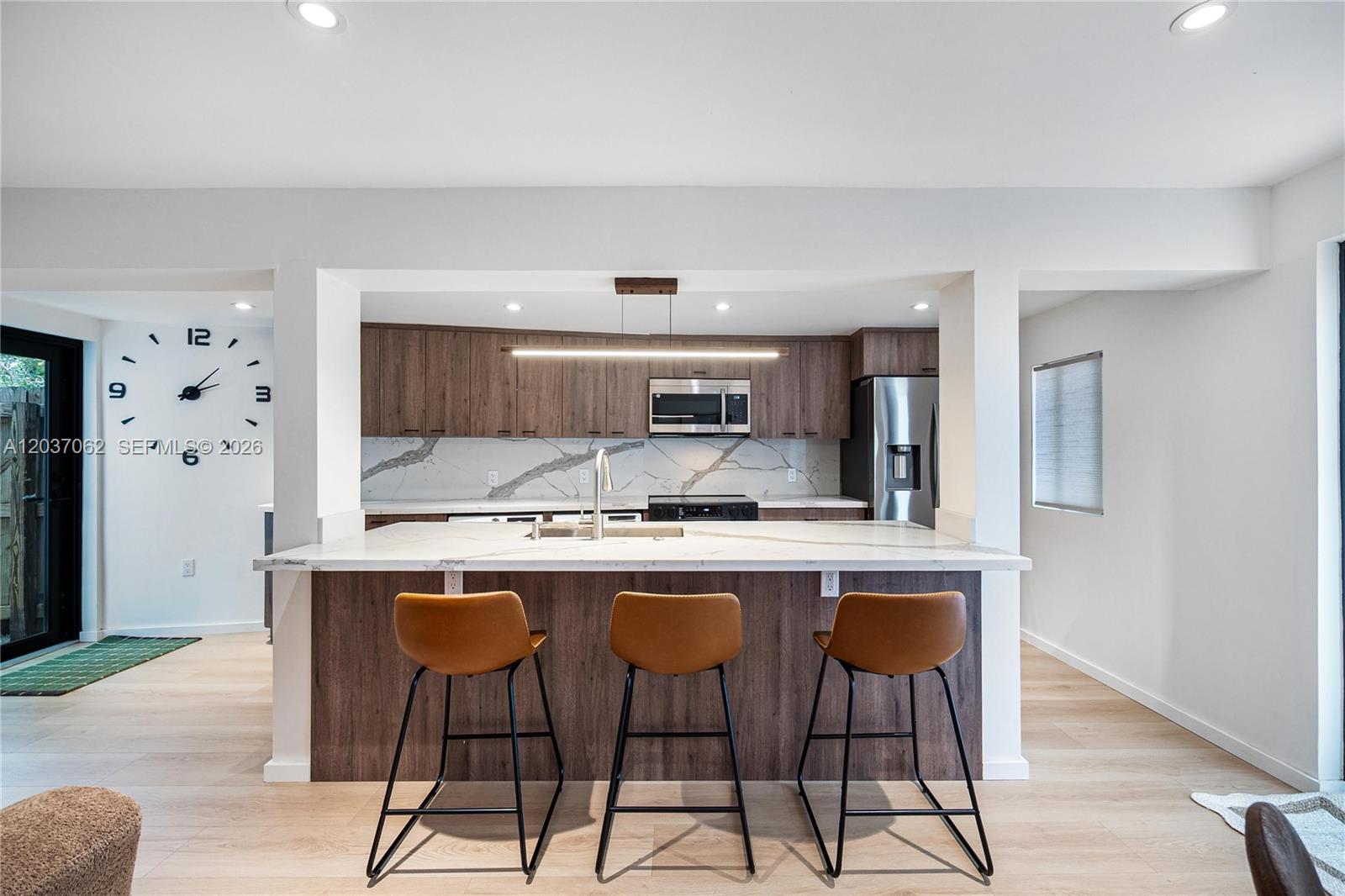A modern kitchen features a marble-topped island with three stools and wood-toned cabinetry — 3681 SW 3rd Ave # 3681, Miami FL 33145, MIAMI, FL