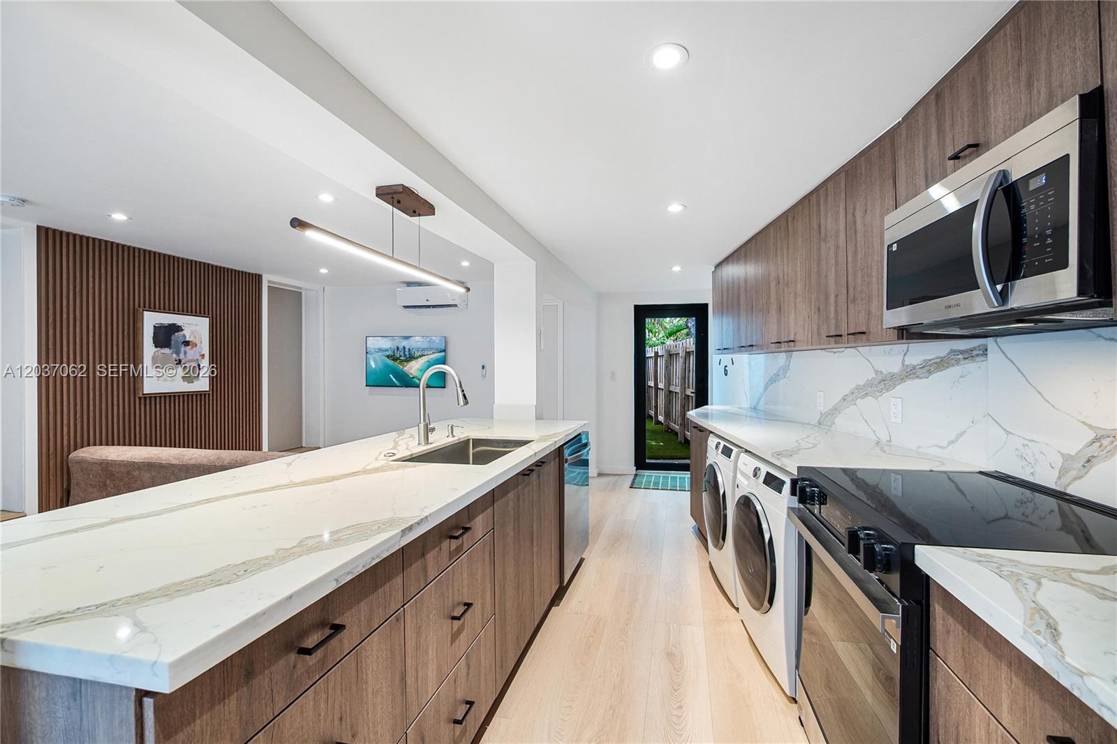A modern kitchen features wood-grain cabinetry, white marble countertops, and integrated laundry appliances — 3681 SW 3rd Ave # 3681, Miami FL 33145, MIAMI, FL