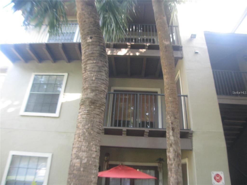 A multi-story apartment building exterior features balconies, palm trees, and a red patio umbrella — 199 AFTON SQUARE UNIT 210, ALTAMONTE SPRINGS, FL