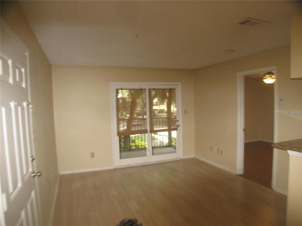 An empty room features light wood-look flooring, a sliding glass door, and a doorway — 199 AFTON SQUARE UNIT 210, ALTAMONTE SPRINGS, FL
