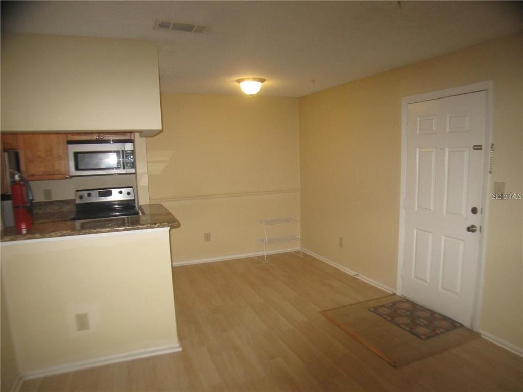 A kitchen with light wood flooring, beige walls, and an adjacent entry door — 199 AFTON SQUARE UNIT 210, ALTAMONTE SPRINGS, FL