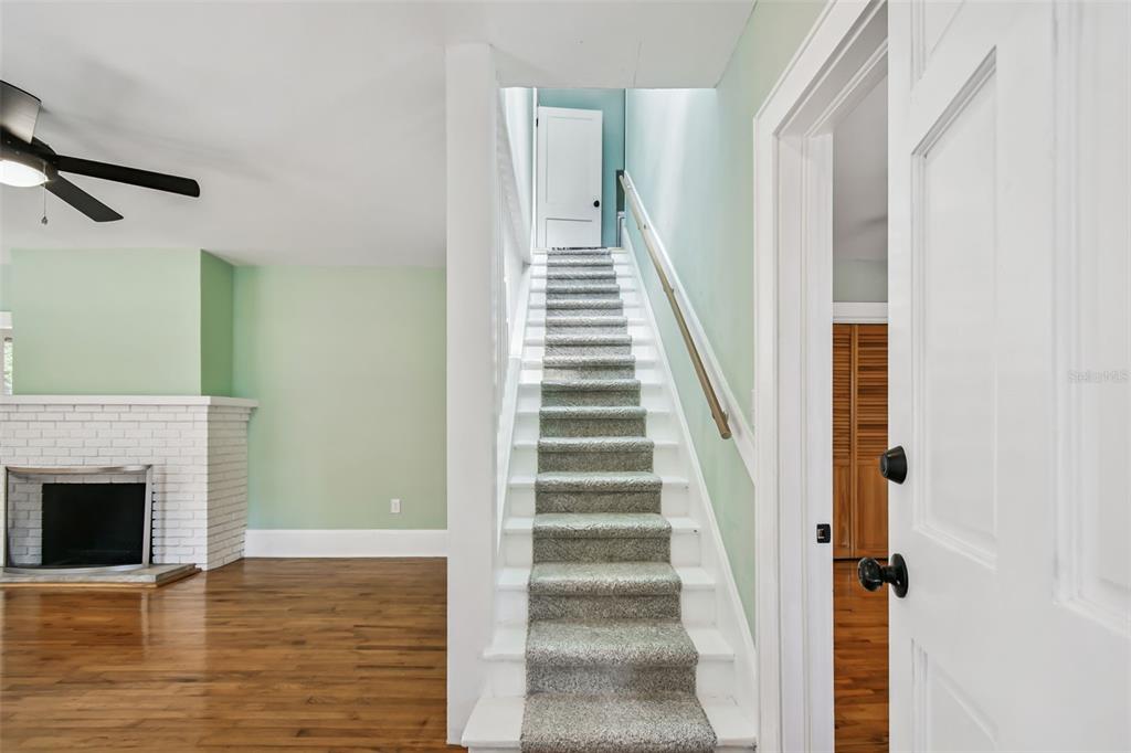 A carpeted staircase leads to an upper floor next to a living room with fireplace — 758 WOOD STREET, DUNEDIN, FL