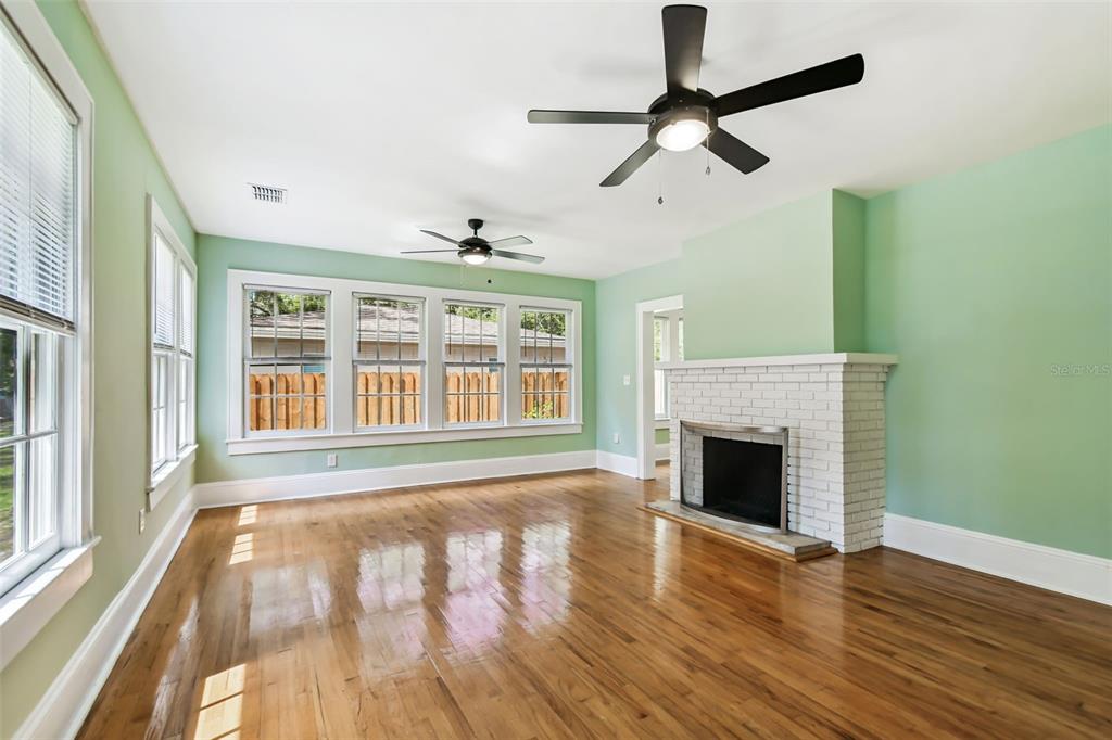 A living room with light green walls, hardwood floors, a white brick fireplace, and ceiling fans — 758 WOOD STREET, DUNEDIN, FL