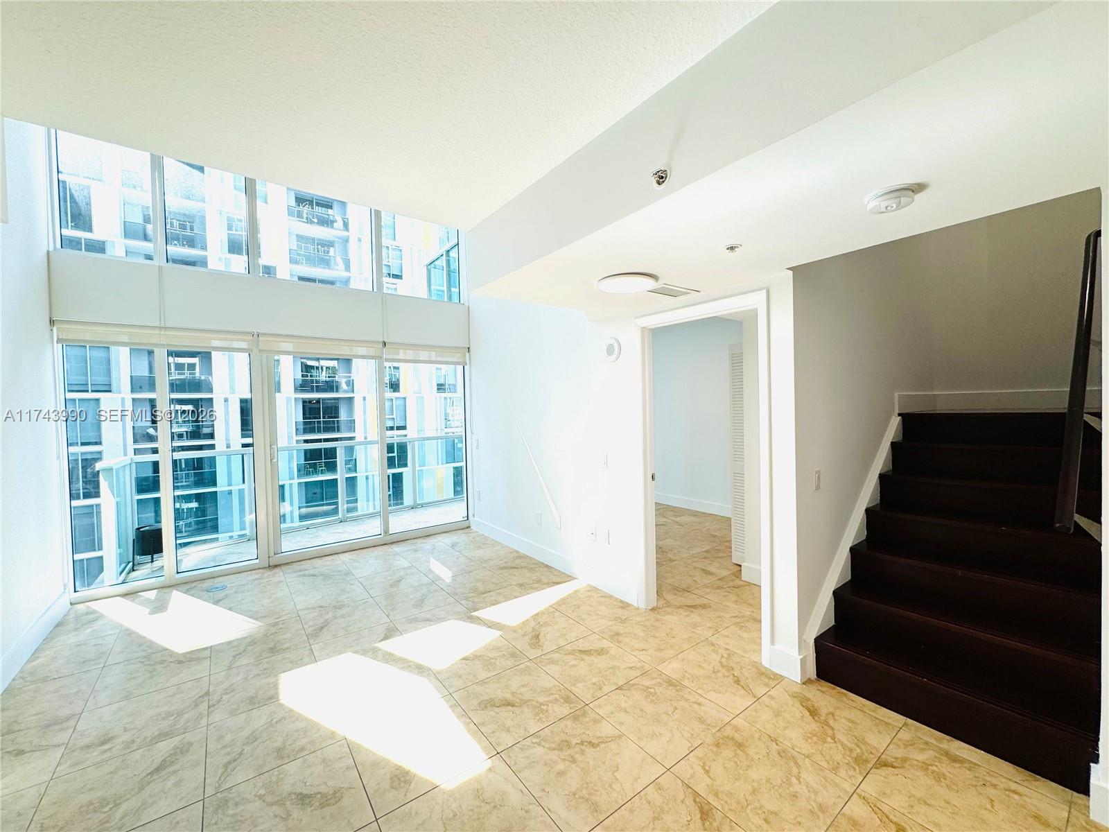 A bright living area features floor-to-ceiling windows, tile flooring, and a staircase leading upward — 41 SE 5th St # 808, Miami FL 33131, MIAMI, FL