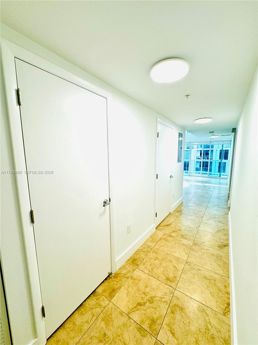 A hallway with white doors, light-colored tile flooring, and recessed ceiling lights leads to windows — 41 SE 5th St # 808, Miami FL 33131, MIAMI, FL