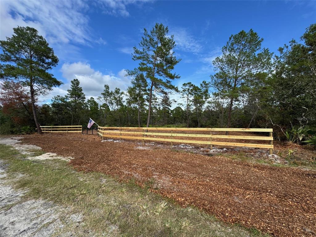 A wooden split-rail fence borders a cleared lot with pine trees and an American flag — KENTUCKY STREET, PAISLEY, FL