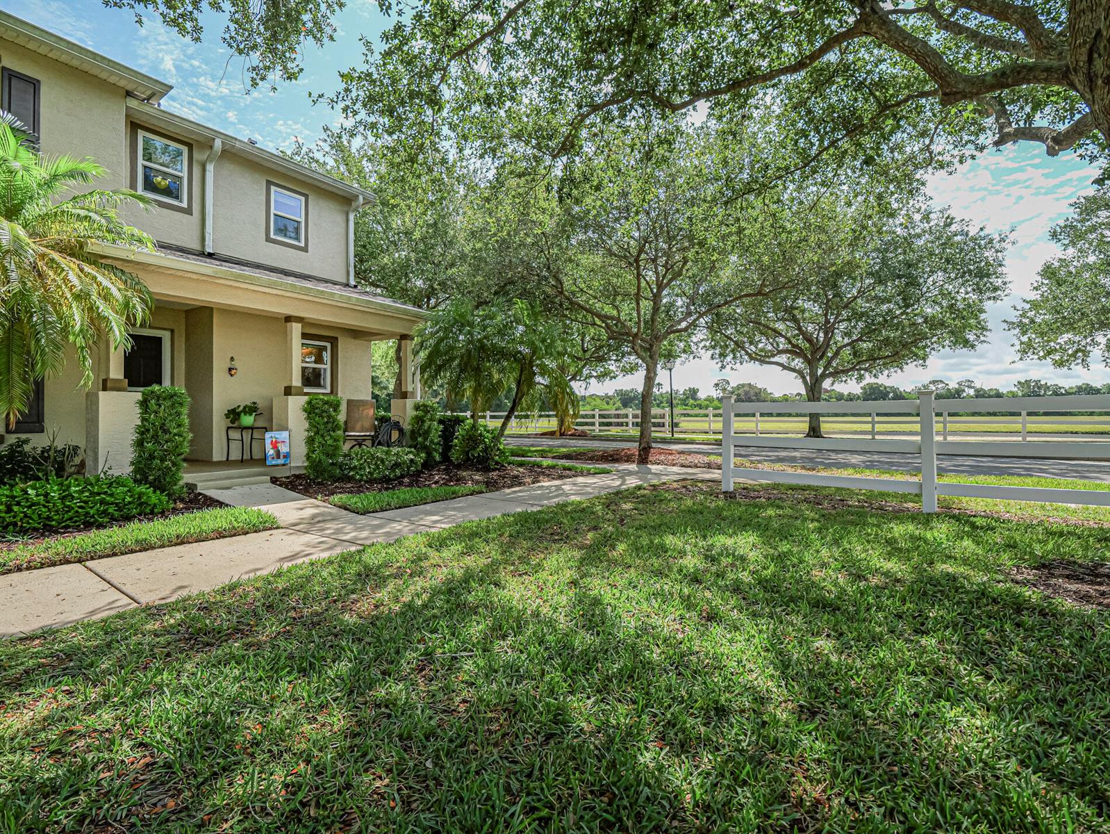 A two-story house with a front porch, lawn, and white fence under large trees — 1838 Pointe West Way, Vero Beach FL 32966, VERO BEACH, FL