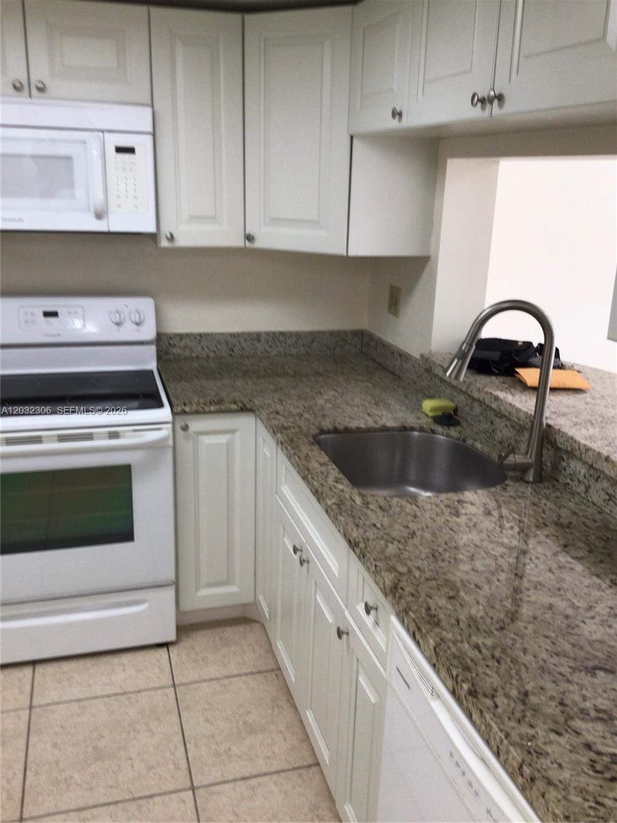 A kitchen features white cabinets, granite countertops, a stainless steel sink, and white appliances — 10975 SW 107th St # 302, Miami FL 33176, MIAMI, FL